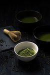 Still life of matcha tea preparation with whisk and bowls of matcha tea and tea powder, low key