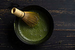 Still life of matcha tea preparation with whisk in bowl of matcha tea, overhead view, low key