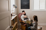 Girl in living room showing book to father and baby brother