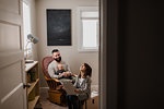 Young man with baby son on lap, laughing with daughter in living room