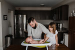 Young man bathing baby son while daughter watches in kitchen