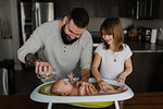 Young man and daughter bathing baby son in kitchen