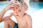 Blond haired boy in swimming shorts sitting at hotel poolside with eyes closed, selective focus, Las Vegas, Nevada, USA