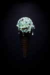 Chocolate chip mint ice-cream cone with melted droplets against black background