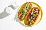 Two garnished hotdogs on yellow plate, overhead still life