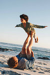 Father lifting son in mid air with legs on beach