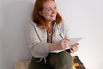 Young woman with red hair sitting holding diary and laughing