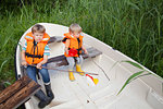 Brothers playing on boat moored in grass field