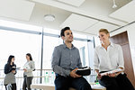 Businessman with VR headset and businesswoman talking in office, colleagues in background