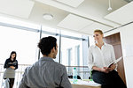 Businessman and businesswoman talking in office, colleague in background