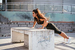 Young woman doing plank on concrete bench