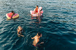 Friends swimming and relaxing on floats on sea, Italy