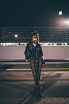 Woman leaning against railing, fencing and floodlights in background, Milan, Italy