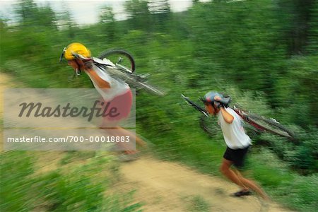 Two People Carrying Mountain Bikes Up Hill