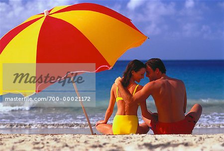 Vue arrière du Couple en maillot de bain assis sur la plage avec parasol