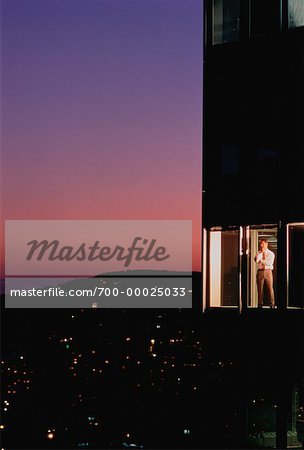 Businessman Standing in Office Tower Window at Dusk