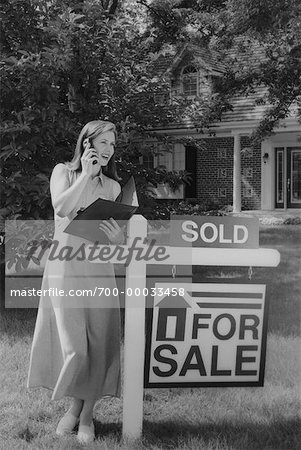 Woman Using Cell Phone near House With For Sale Sign