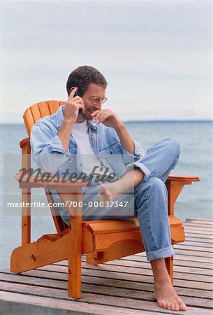 Mann sitzt im Stuhl auf Dock mit Handy