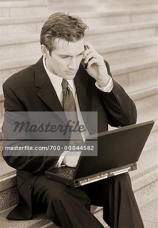 Businessman Sitting on Steps Using Cell Phone and Laptop Computer Outdoors