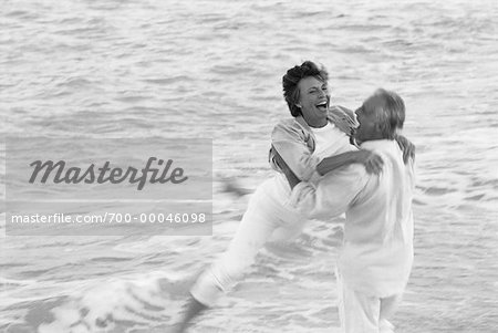 Mature Couple Embracing in Surf On Beach