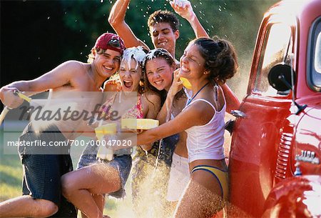 Group of Teenagers in Water Fight While Washing Truck