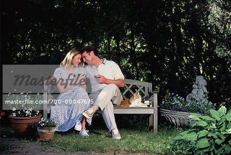 Couple tenant des verres à vin assis sur un banc avec chat en plein air