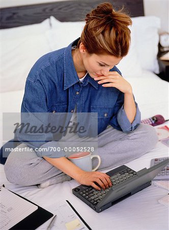 Femme assise sur le lit à l'aide d'ordinateur portable