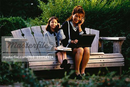 Mère et fille en complet-veston avec les téléphones cellulaires sur le banc