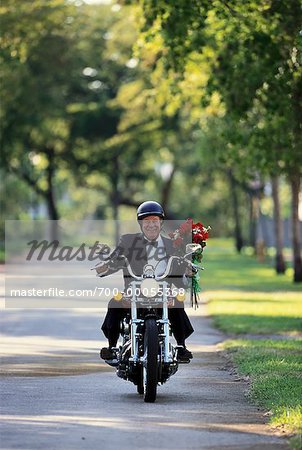 Mature Man Riding Motorcycle Carrying Bouquet of Flowers