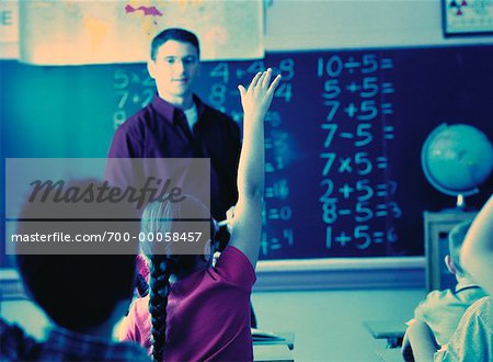 Male Teacher Looking at Girl With Hand Raised in Classroom