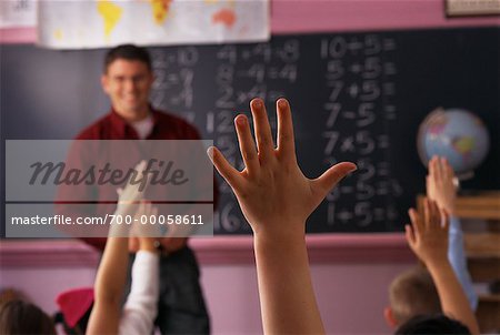 Male Teacher Looking at Children With Hands Raised in Classroom