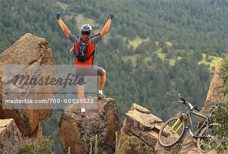 Homme debout sur le rocher, les bras levés, avec vue sur la forêt