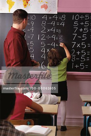 Back View of Male Teacher with Girl Writing on Blackboard