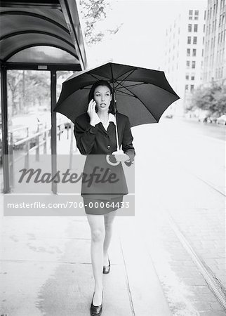 Geschäftsfrau zu Fuß auf der Straße mit Regenschirm, mit Handy