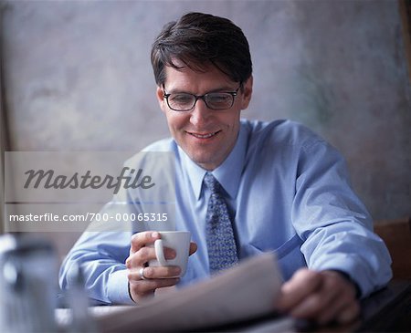 Homme d'affaires détenant journal lecture tasse à café au bureau