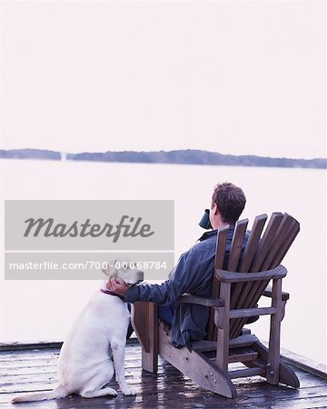 Man Sitting in Adirondack Chair On Dock with Dog Bala, Ontario, Canada