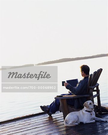 Man Sitting in Chair on Dock With Laptop, Mug and Dog Bala, Ontario, Canada