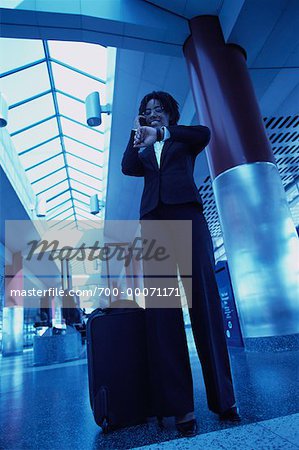 Businesswoman Standing in Terminal, Checking Watch, Using Cell Phone