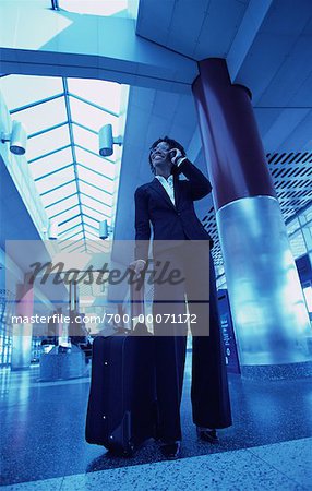 Businesswoman Standing in Terminal with Luggage, Using Cell Phone