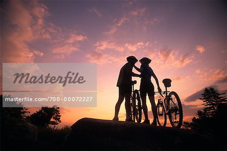 Couple Standing on Rock with Mountain Bikes at Sunset