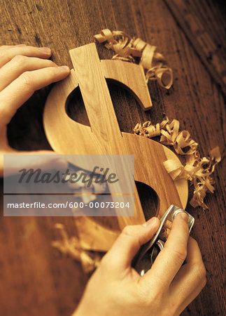 Close-Up of Hands Carving Wooden Dollar Sign