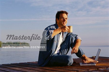 Homme assis sur le quai avec ordinateur portable et Mug