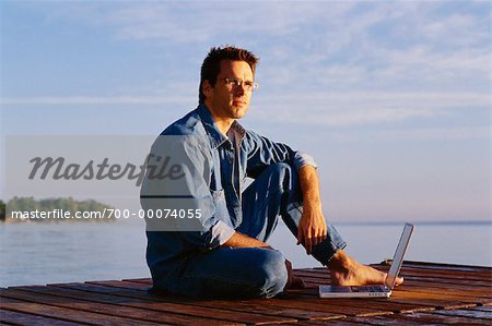 Portrait d'un homme assis sur le quai avec ordinateur portable