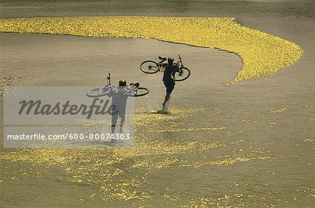 Couple transportant des vélos à travers l'eau, Milk River, Alberta, Canada