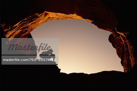 Silhouette de personne assis sous l'arche au coucher du soleil Arches National Park, Utah, Etats-Unis