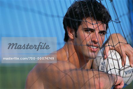 Portrait of Man Leaning on Net Holding Volleyball Outdoors