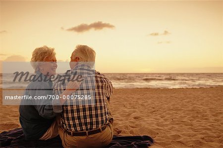 Back View of Mature Couple Sitting on Beach at Sunset