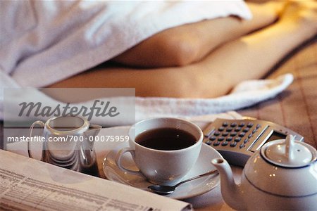 Woman Lying on Hotel Bed in Bathrobe with Financial Pages and Tea Service