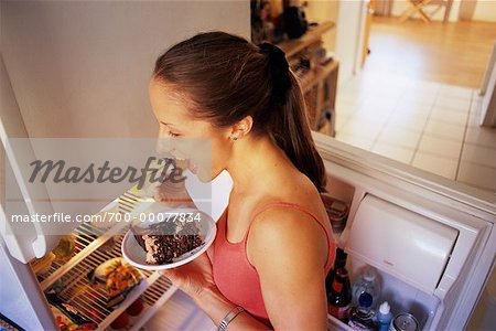 Femme se tenant près de réfrigérateur manger un gâteau au chocolat