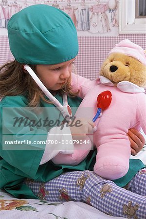Mädchen sitzen auf dem Bett in Arzt Kostüm, spielen Arzt mit Teddybär